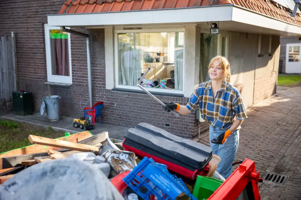 Vrouwelijke klusser gooit een stuk puin in een puincontainer
